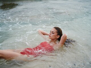 Woman lying on the ocean on the beach in the waves in a red swimsuit, a hotel vacation