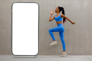Fototapeta na wymiar Sportswoman doing fitness in front of big giant smartphone with blank white screen on gray background presenting new cool app, free copy space mockup, website design banner