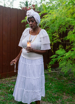Woman in garden praying with candle and rosary
