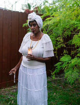 Woman in garden praying with candle and rosary