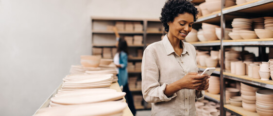 Smiling ceramist using a smartphone in her shop