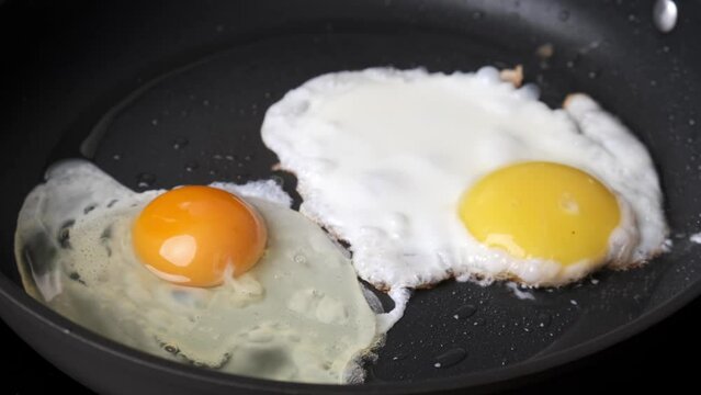 Frying egg in black frying pan. Breakfast preparation process.