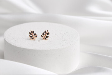 Subject shot of two gold earrings shaped as leaves on concrete podium. Beautiful accessories for...