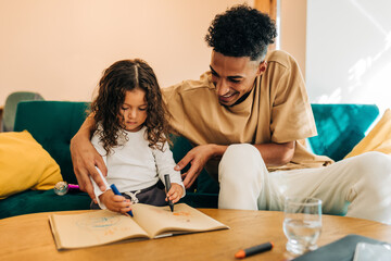 Fototapeta premium Cheerful single father teaching his daughter how to draw in a colouring book