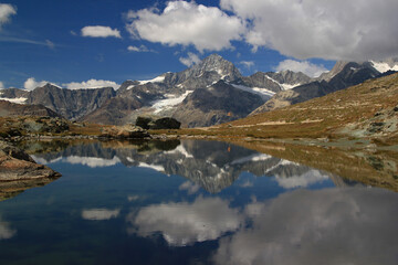 Fototapeta na wymiar A landscape with a smooth Riffelsee lake surface and mountains and clouds reflected in it, on a mountain Gornergrat, near Zermatt, in southern Switzerland