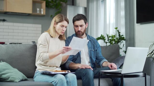 Unhappy young couple opening envelope with letter about financial problem bank debt bill or medical results sitting on the couch in the living room at home Upset family received bad news by mail
