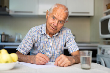 Man writing letter on paper while sitting in kitchen at home