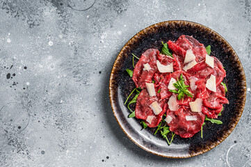 Delicious veal carpaccio with Parmesan cheese, spices and herbs. Gray background. Top view. Copy...
