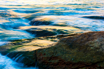 Sea water blurred by the movement and dripping between the stones with the colors and brightness of the sunset on Ipanema beach in Rio de Janeiro