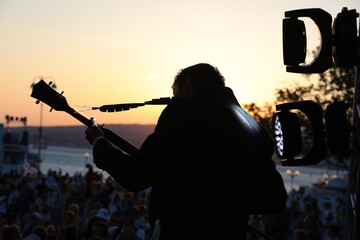 Silhouette of a person with a guitar playing at sunset outdoors