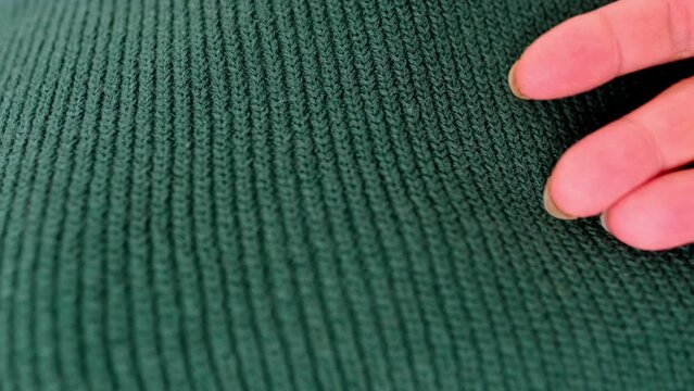 close-up of female hand touches knitted jersey, embossed canvas, green wool yarn, knitted texture, concept of warm things for cold weather, check quality, fashionable clothes, clothing production
