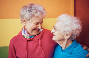 Friends, happy and retirement with a senior woman and friend outdoor together on a color wall...