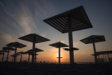Silhouettes of wooden beach umbrellas at sunset on the sea beach.