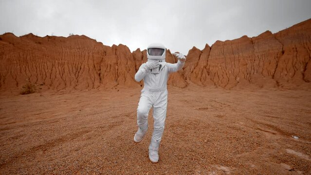 An astronaut dances to the surface of Mars in slow motion. Astronauts in a white space suit and helmet are very excited about their exploratory journey to a distant planet.