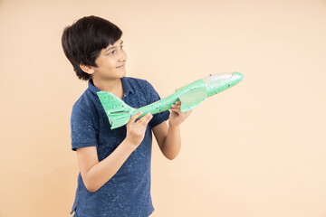 Happy playful indian boy kid holding airplane toy in hand isolated on beige studio background. copy...