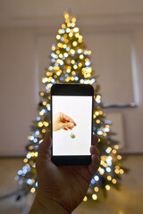 Man taking picture of Christmas tree decorated with a mobile phone