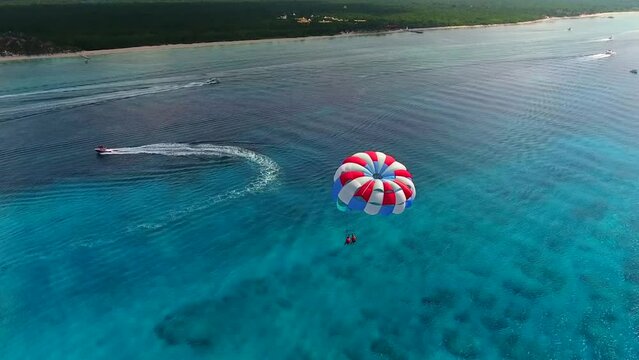 Parasailing aerial view. A couple paraskiing at tropical beach in bright day. 