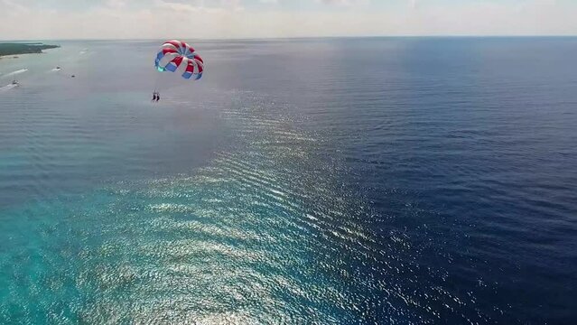 Parasailing aerial view. A couple paraskiing at tropical beach in bright day. 