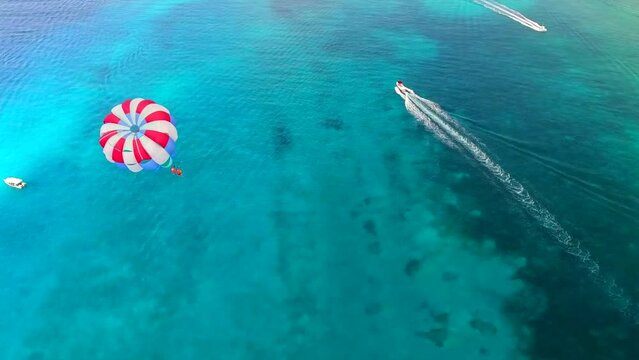 Parasailing aerial view. A couple paraskiing at tropical beach in bright day. 