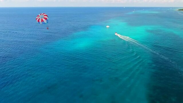 Parasailing aerial view. A couple paraskiing at tropical beach in bright day. 