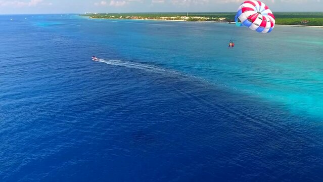 Parasailing aerial view. A couple paraskiing at tropical beach in bright day. 