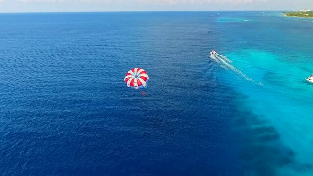 Parasailing aerial view. A couple paraskiing at tropical beach in bright day. 