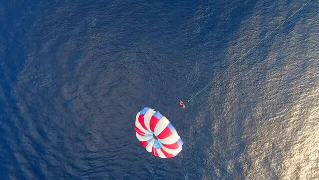 Parasailing aerial view. A couple paraskiing at tropical beach in bright day. 