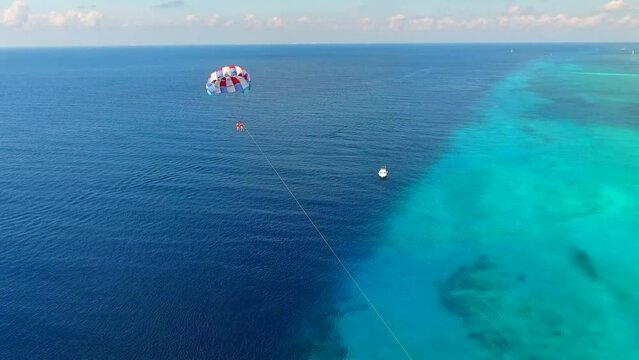 Parasailing aerial view. A couple paraskiing at tropical beach in bright day. 