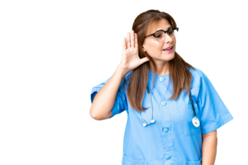 Middle age nurse woman over isolated background listening to something by putting hand on the ear