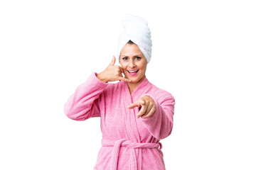 Middle age caucasian woman in a bathrobe over isolated background making phone gesture and pointing front