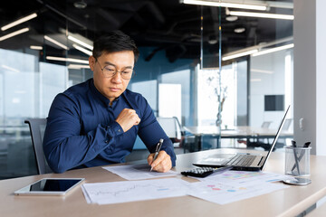 Serious thinking asian man working with documents inside office, concentrated businessman with contracts and bills reading and calculating reports, mature financier with documents. - Powered by Adobe