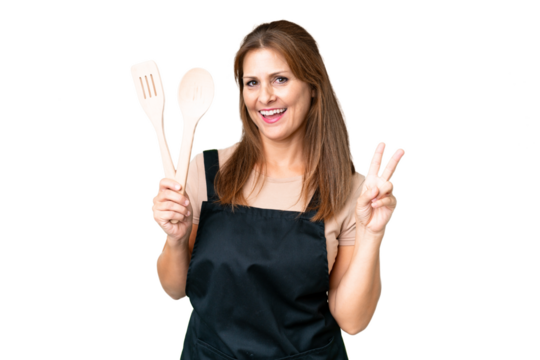 Middle age caucasian woman holding a rolling pin over isolated background smiling and showing victory sign - Powered by Adobe