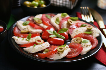 Caprese salad with mozzarella and tomatoes on black plate and table