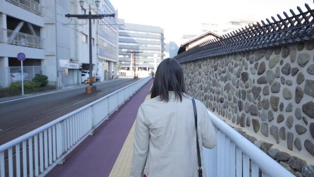 Back shot of asian girl walking by the stone wall in Nagasaki Japan.