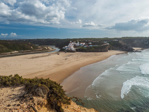 Panoramic view of Praia de Odeceixe Mar Surfer beach with golden sand, atlantic ocean waves, river bend and white houses of Odeceixe village. Rota Vicentina coast, Odemira, Portugal.