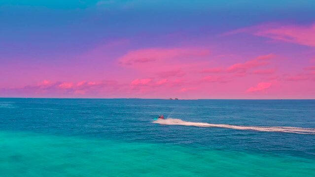 Aerial view of jet ski watercraft cruising in high speed in tropical exotic sea during pink sunset in Maldives.