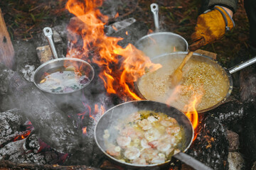 A large pan of shrimp in  is cooked above an open flame set in an outdoor