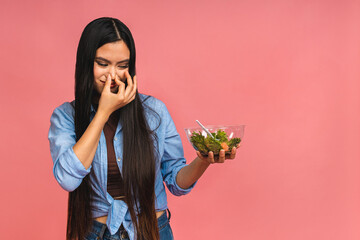 Bad smell of stale food concept. Asian woman holding vegeterian salad or bowl in take away container. Close up, copy space, top view, isolated over pink background.