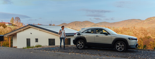 Young woman charging her electric car in home, sustainable and economic transportation concept.