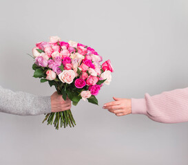 Hand giving reses flowers bouquet to woman on grey background. Valentines or mothers day consept.
