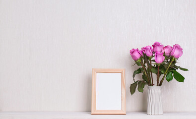 Vase with violet roses and photo frame with copy-space on white background.