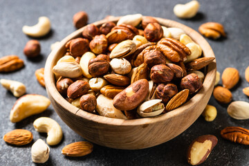 Assortment of nuts in wooden bowl on dark stone table. Cashew, hazelnuts, almonds, brazilian nuts and pecans. Close up.