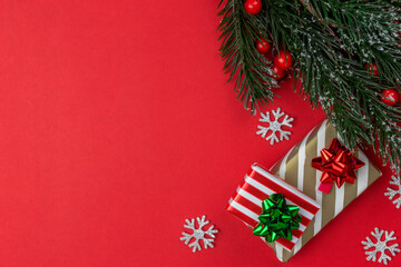 Christmas presents and gifts in red and golden striped paper with christmas tree branch and holly top view on red background with copy space.