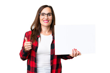Middle age woman over isolated chroma key background holding an empty placard with thumb up