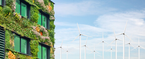 Exterior of a green sustainable building covered with blooming vertical hanging plants in front of wind turbines
