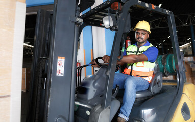 A young professional engineer in a safety helmet works in a warehouse, operates a forklift, checks goods at a warehouse.