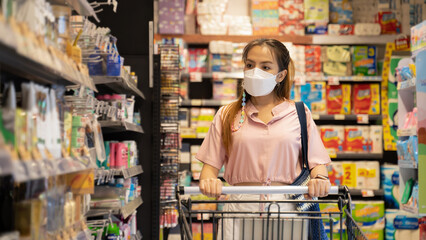 New normal after covid epidemic and shopping concept,young smart Asian woman new lifestyle shoping at supermarket with face shild or mask protection choosing water as new normal lifestyle