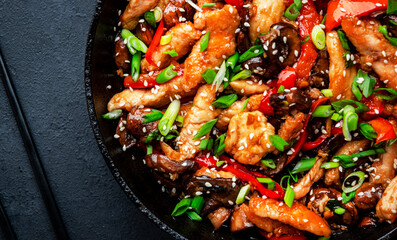 Stir fry with turkey fillet, paprika, mushrooms, green chives and sesame seeds in frying pan. Asian cuisine dish. Black stone kitchen table background, top view