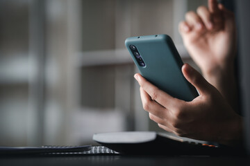 Beautiful Asian woman playing mobile phone in her break from work, she is a marketing manager of a startup company, female leader, supervisor, ceo. Female Leadership Concept.