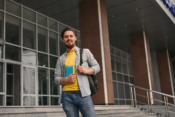 Content bearded guy with backpack standing on stairs of college building